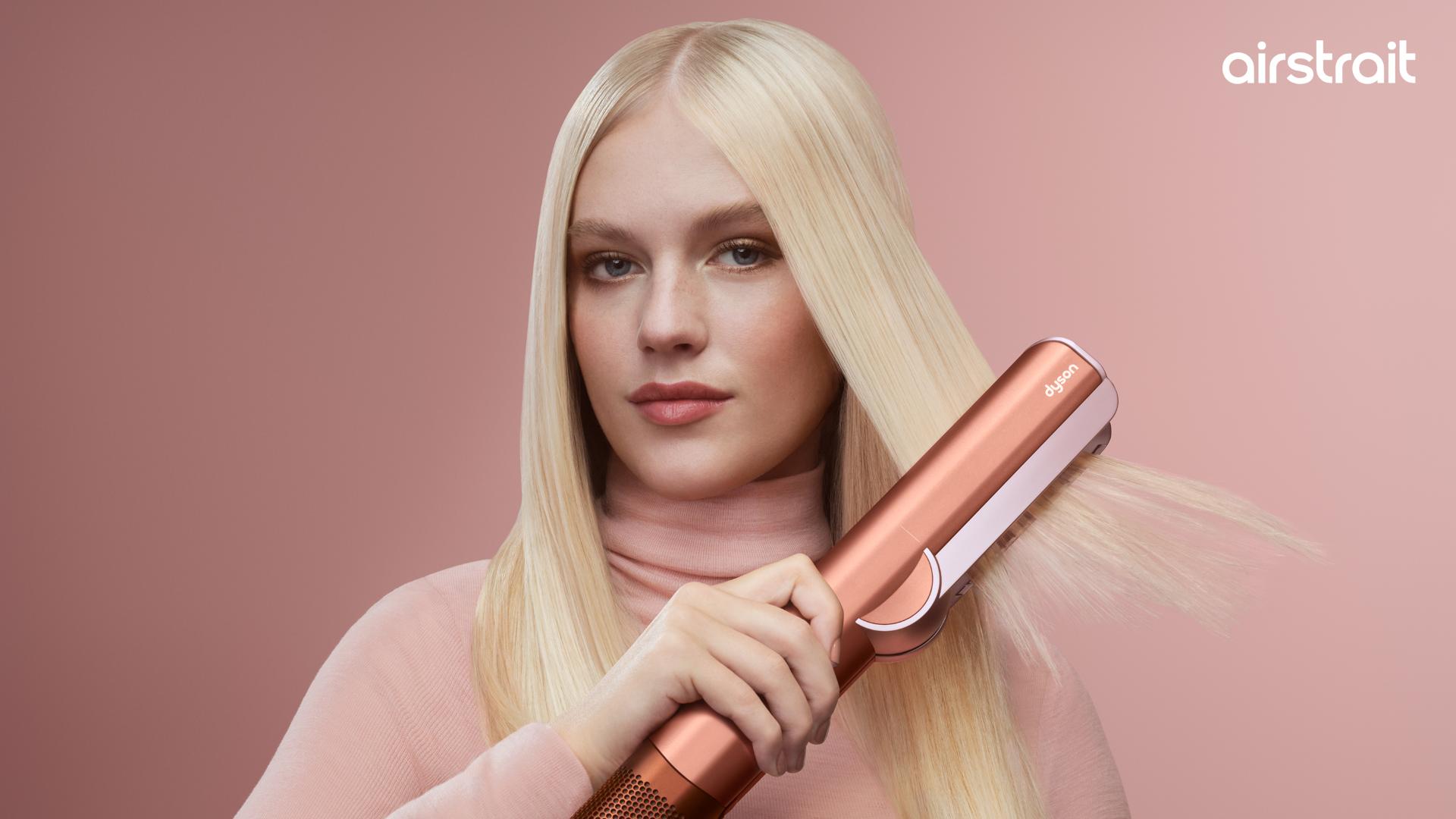 A blonde model dries and styles her hair with the Dyson Airstrait dryer and straightener.