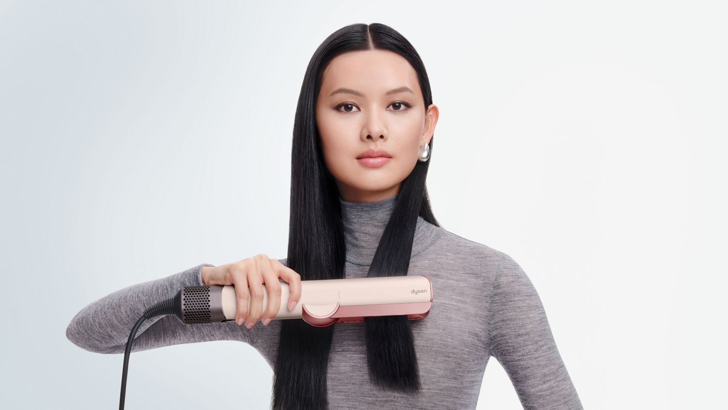 Ein Modell glättet ihr Haar mit dem Dyson Airstrait Haartrockner und -glätter.