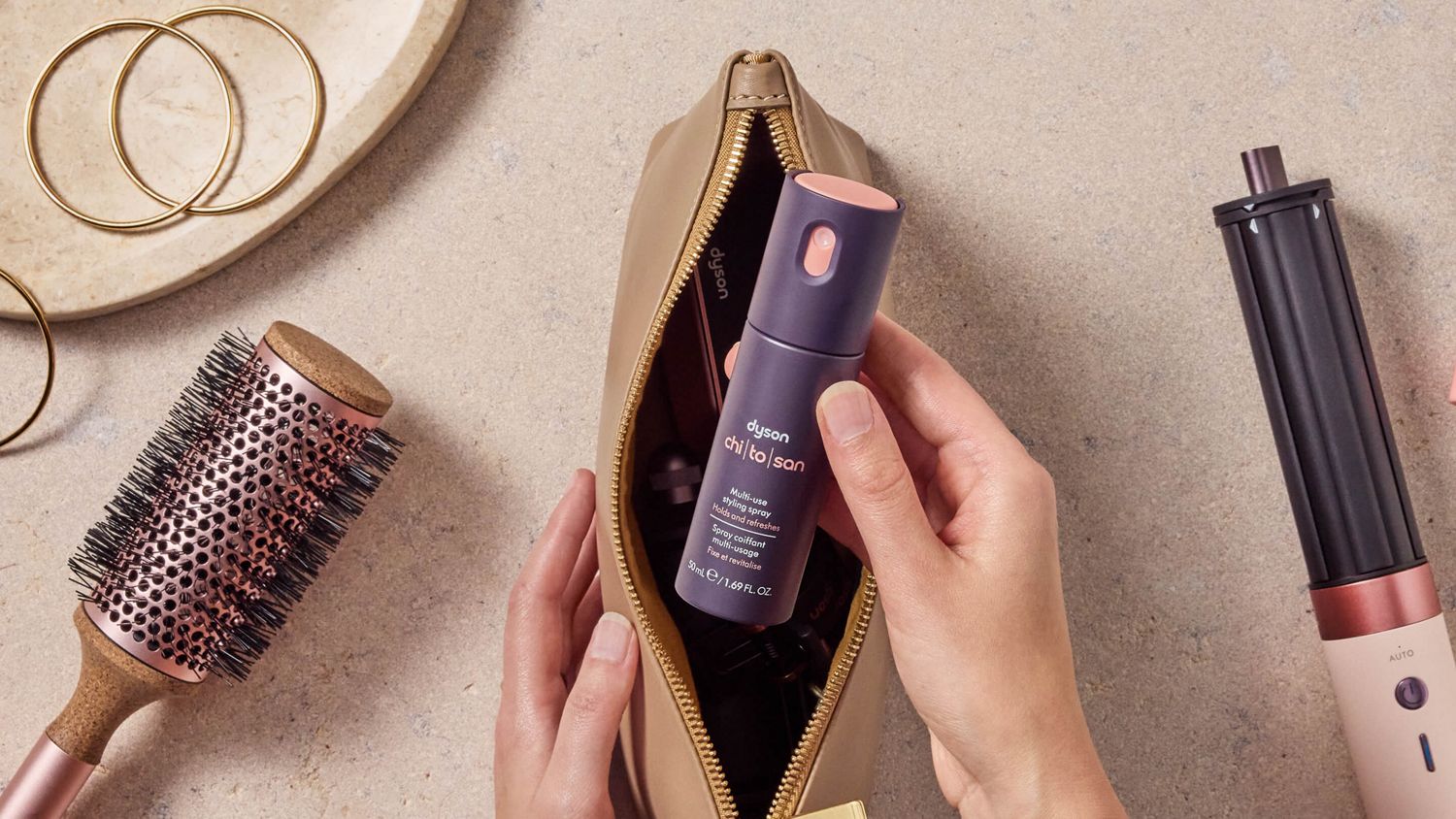 Model holding the Dyson Chitosan Multi-use styling spray in a makeup bag.