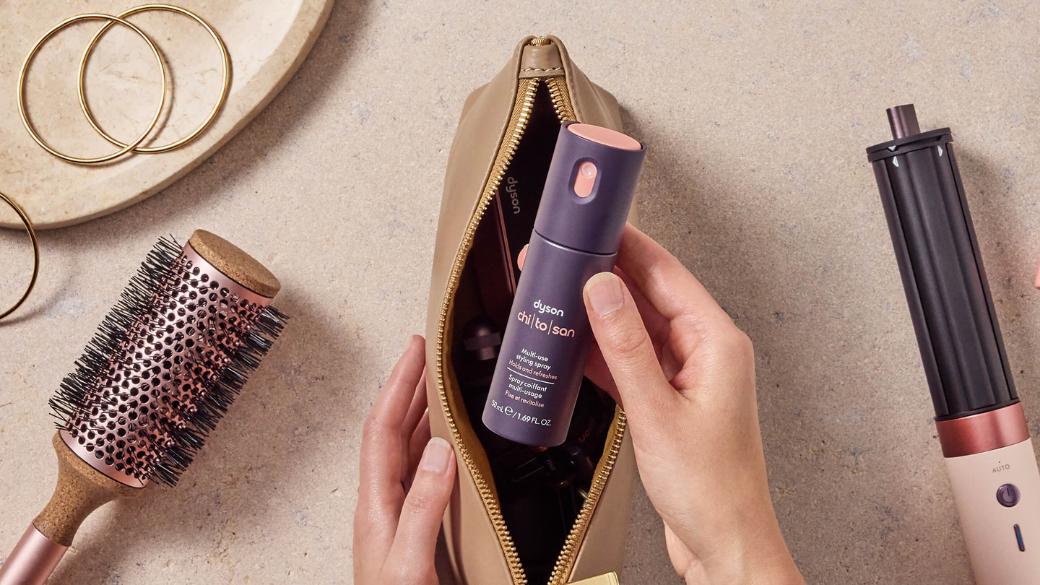 Model holding the Dyson Chitosan Multi-use styling spray in a makeup bag.