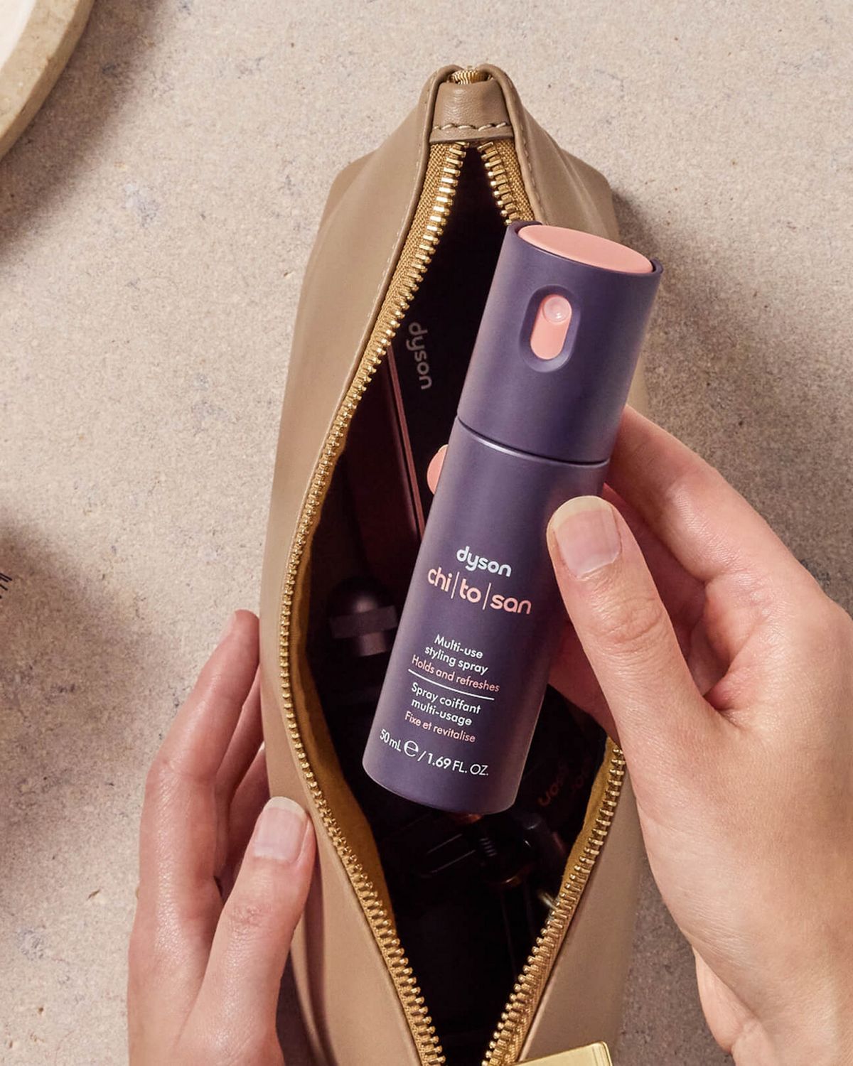Modelo sosteniendo el espray de moldeado multiusos Dyson Chitosan en una bolsa de maquillaje.