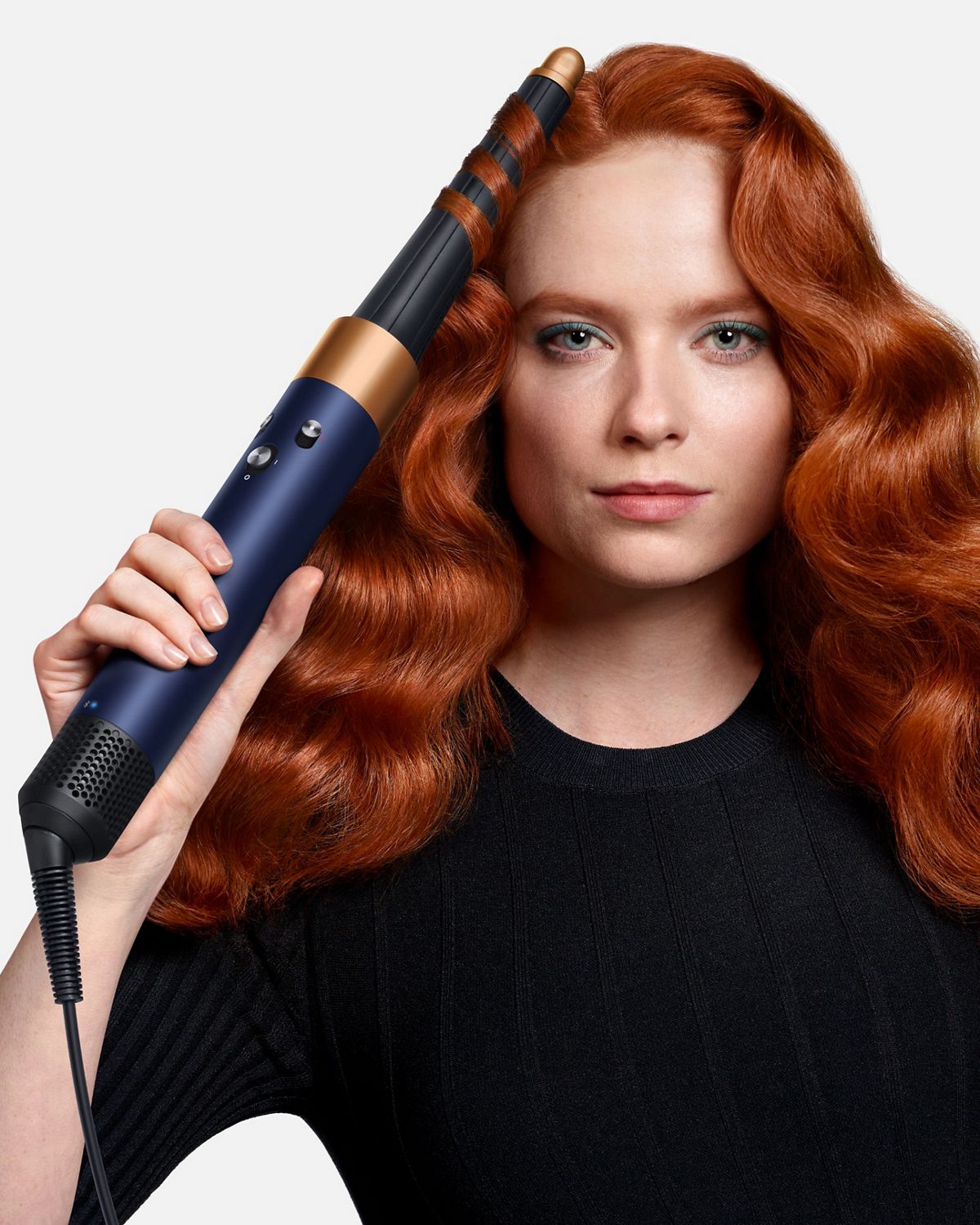 A redhead model adds waves to her hair using the Dyson Airwrap i.d. multi-styler and dryer.