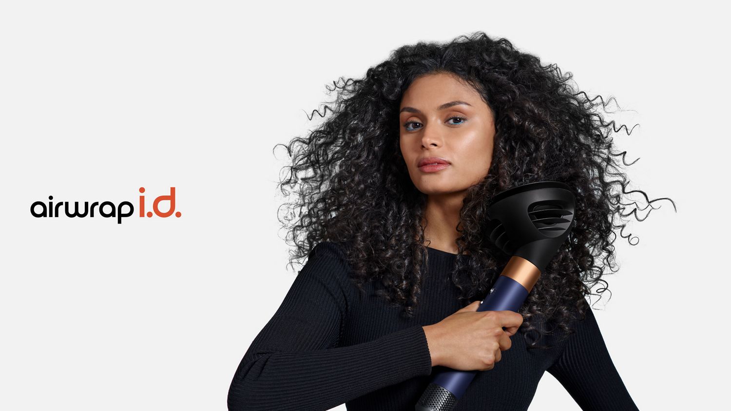 A curly haired model styles her hair using the Dyson Airwrap i.d. multi-styler and dryer and the Wave+Curl diffuser.