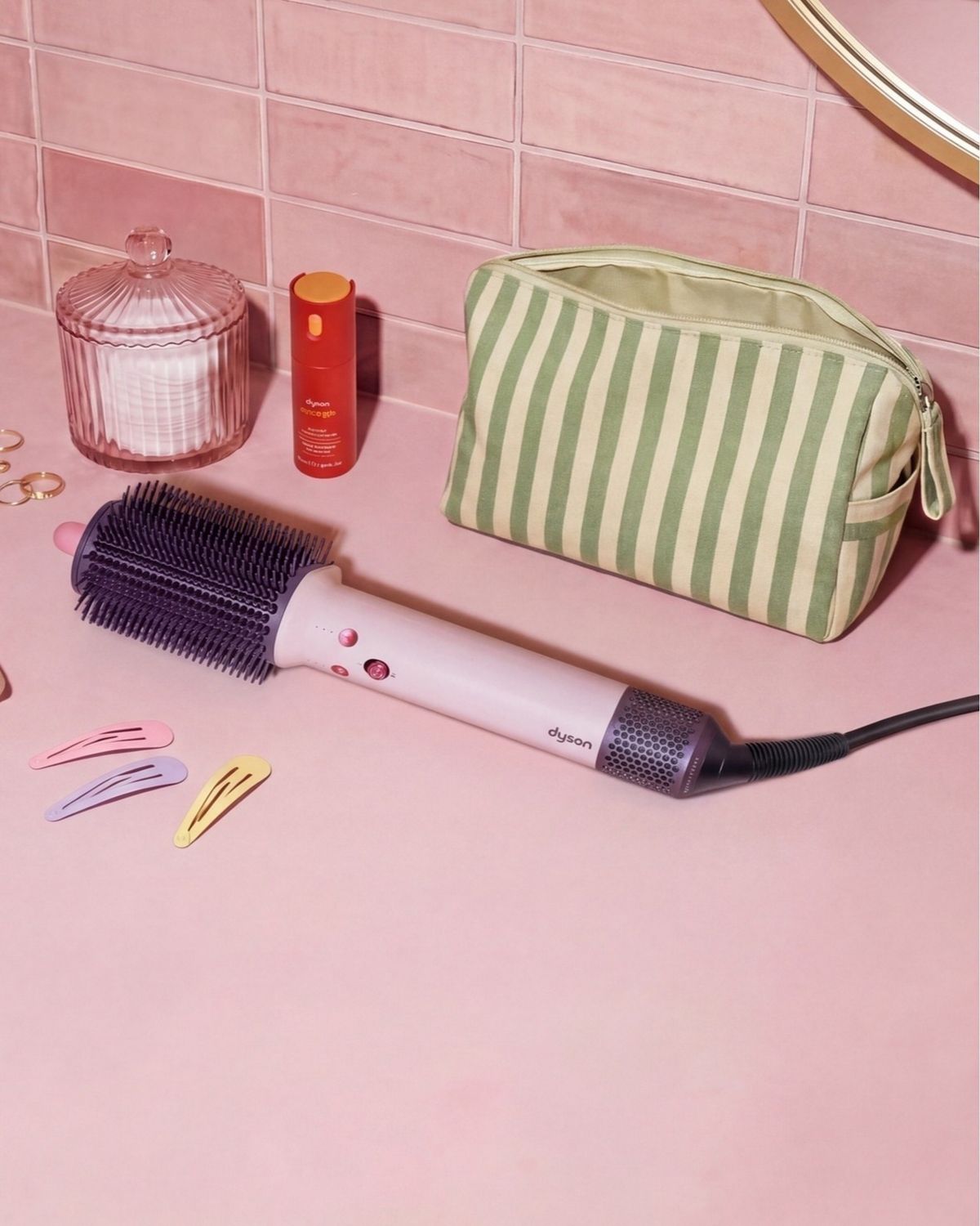 Dyson Airsmooth styling brush next to hair clips and a toiletries bag.