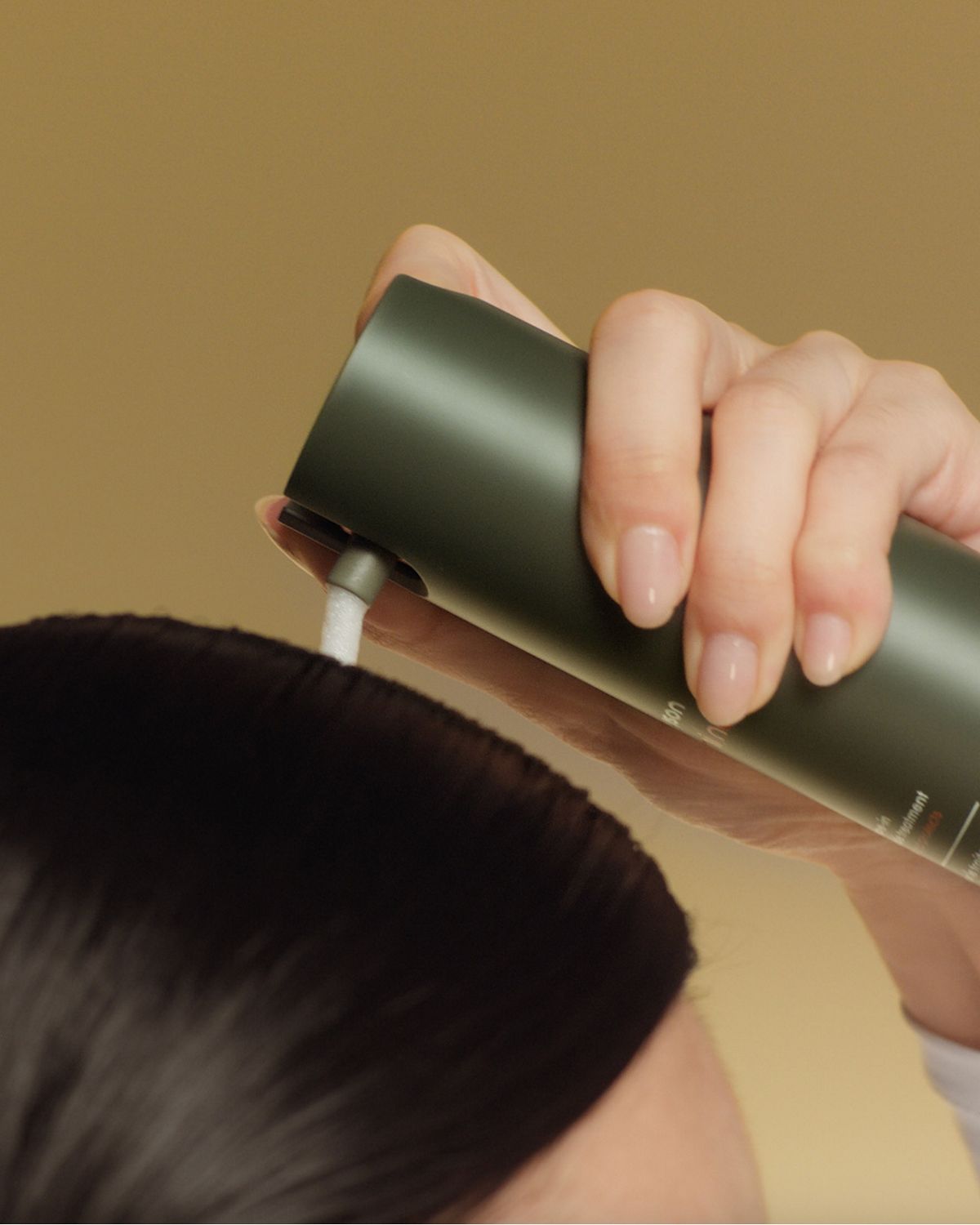 A model applies Dyson Amino leave-in scalp bubble treatment to her scalp.