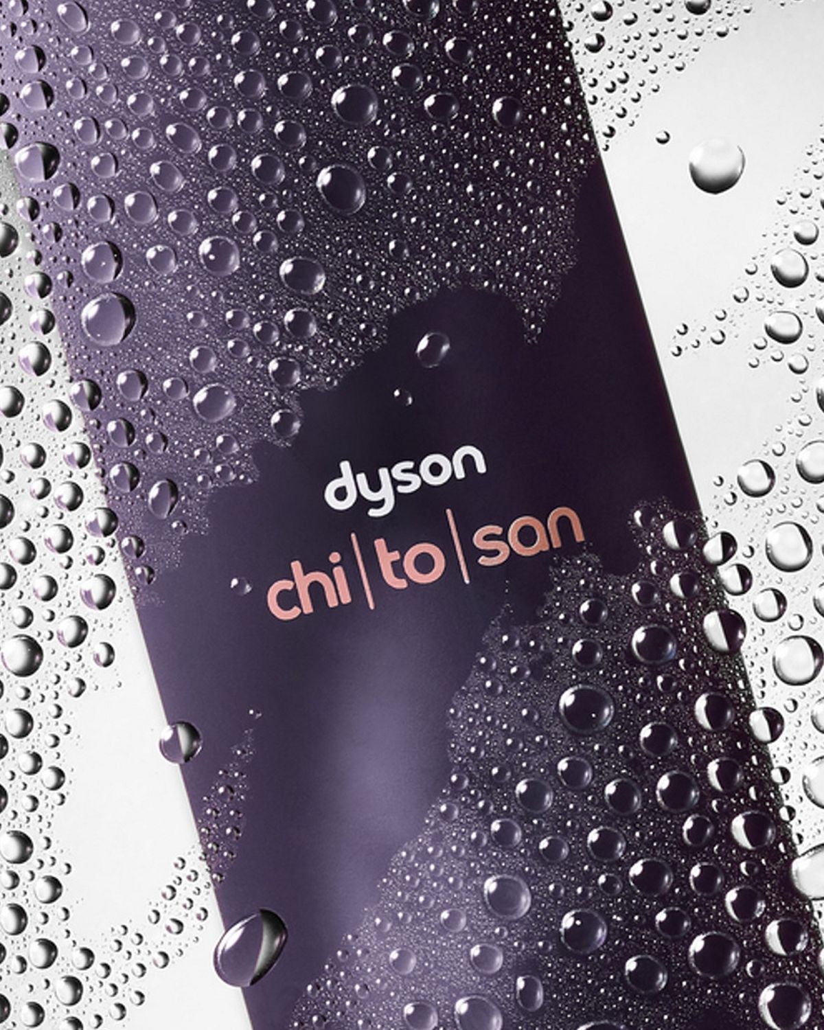 Dyson Chitosan Multi-use styling spray behind water droplets on a glass pane.