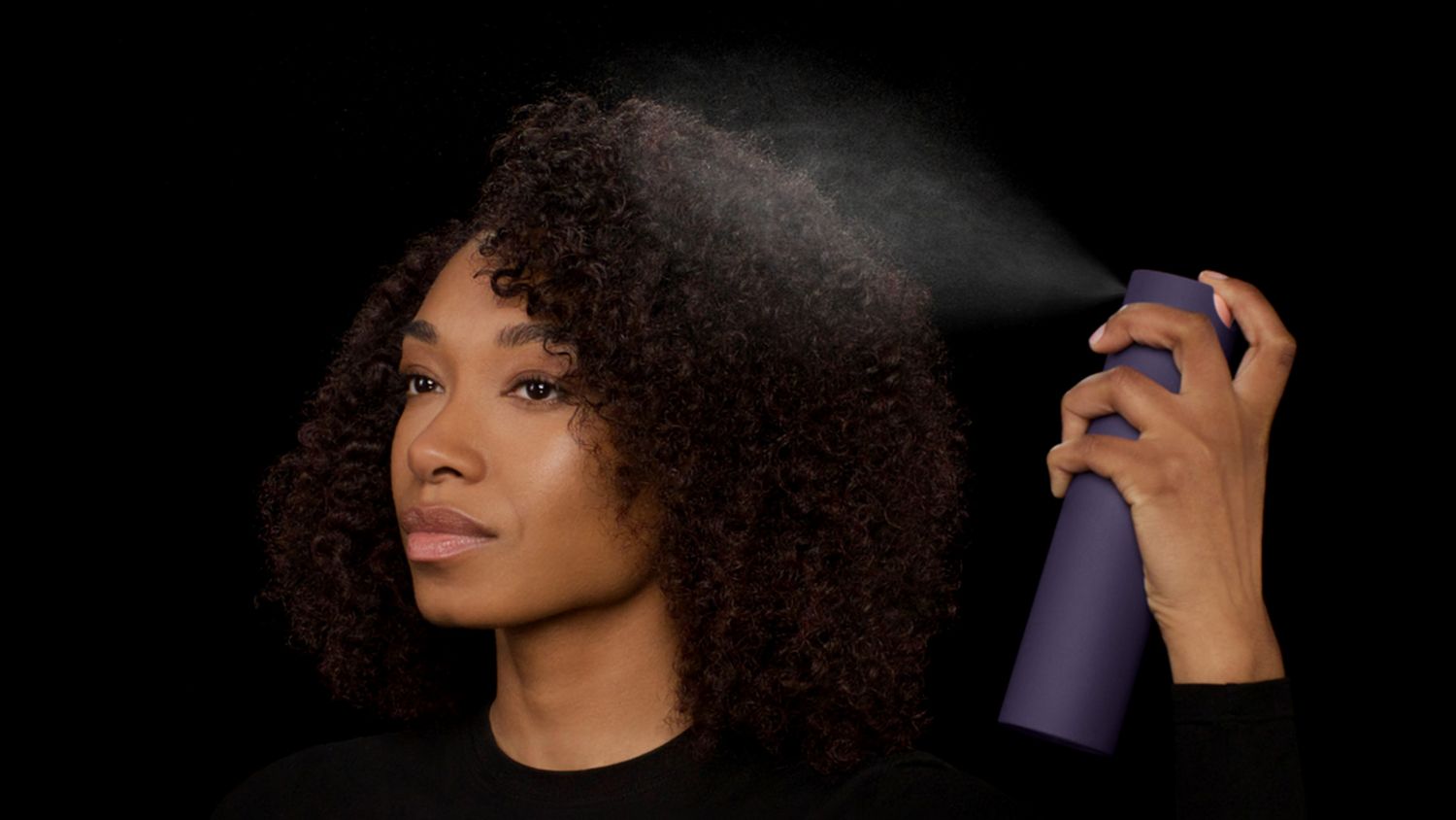 Dyson Chitosan Multi-use styling spray is sprayed onto brown coily hair.