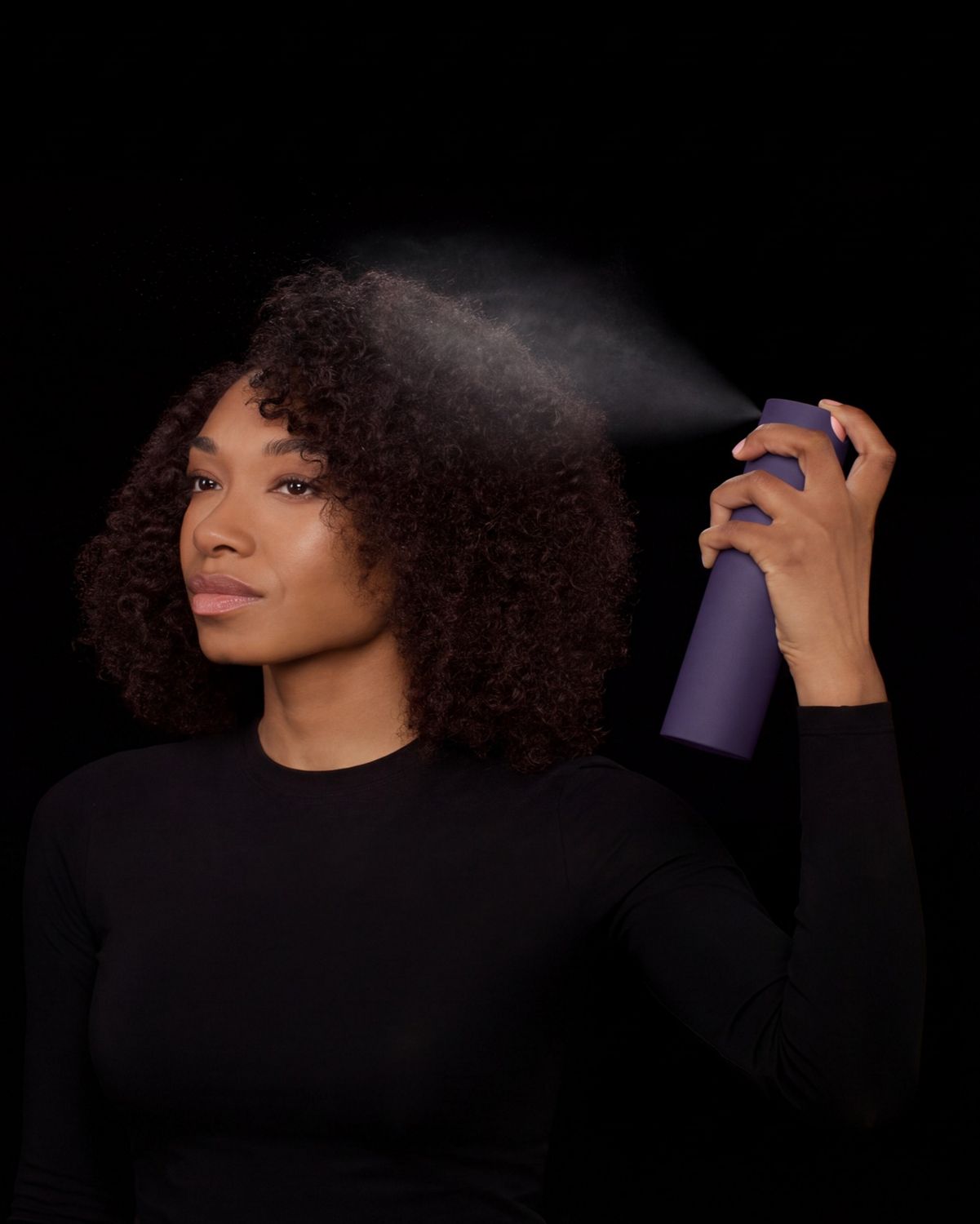 Dyson Chitosan Multi-use styling spray is sprayed onto brown coily hair.