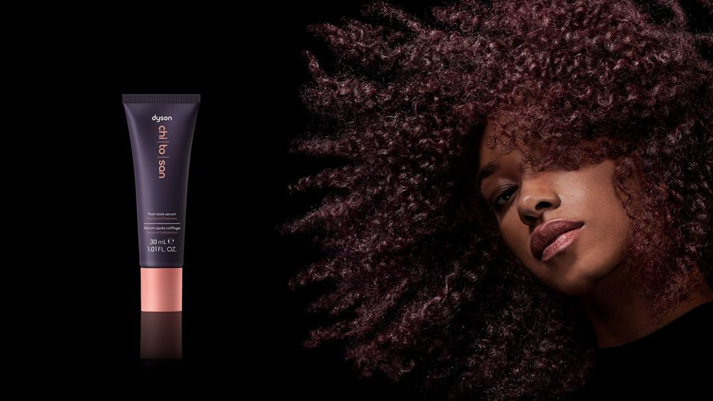 A model with dark coily hair after styling their hair with Dyson Chitosan Post-style serum.