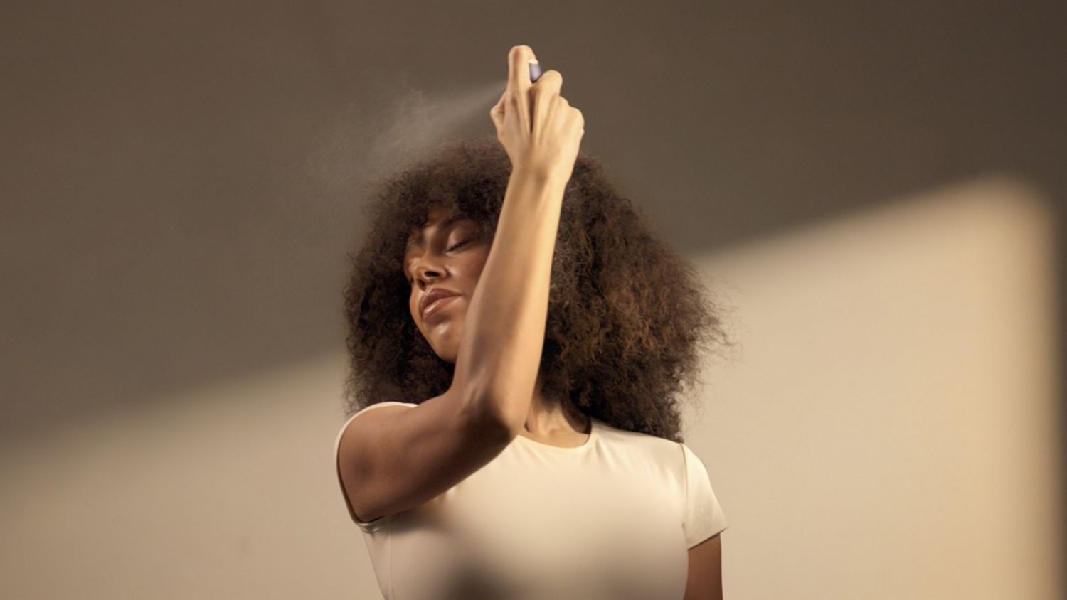 Model spritzes her hair with the Dyson Chitosan Multi-use styling spray travel mini.