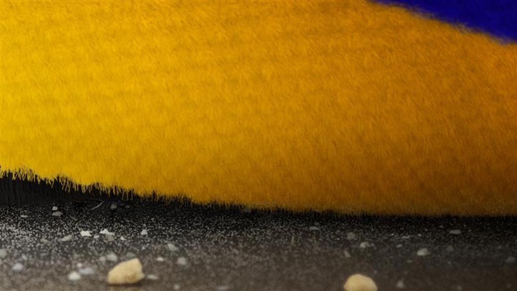 Close-up of the Dyson Fluffy Optic cleaner head’s brush bar as it cleans into a crevice on a hard floor.