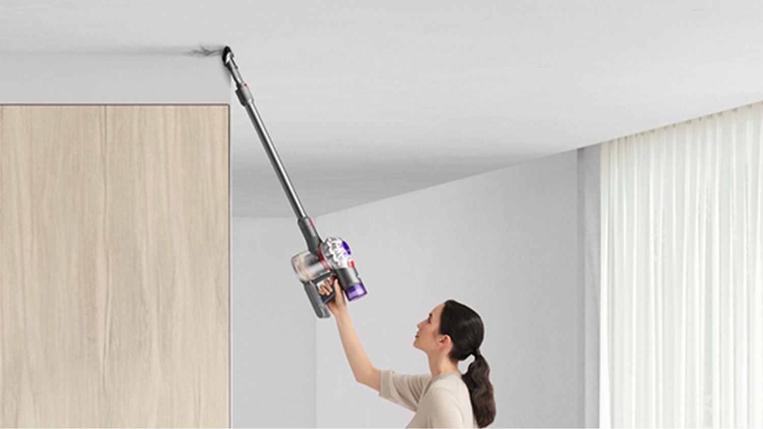 A woman using the Dyson V8 vacuum to clean a ceiling using the Combination tool.