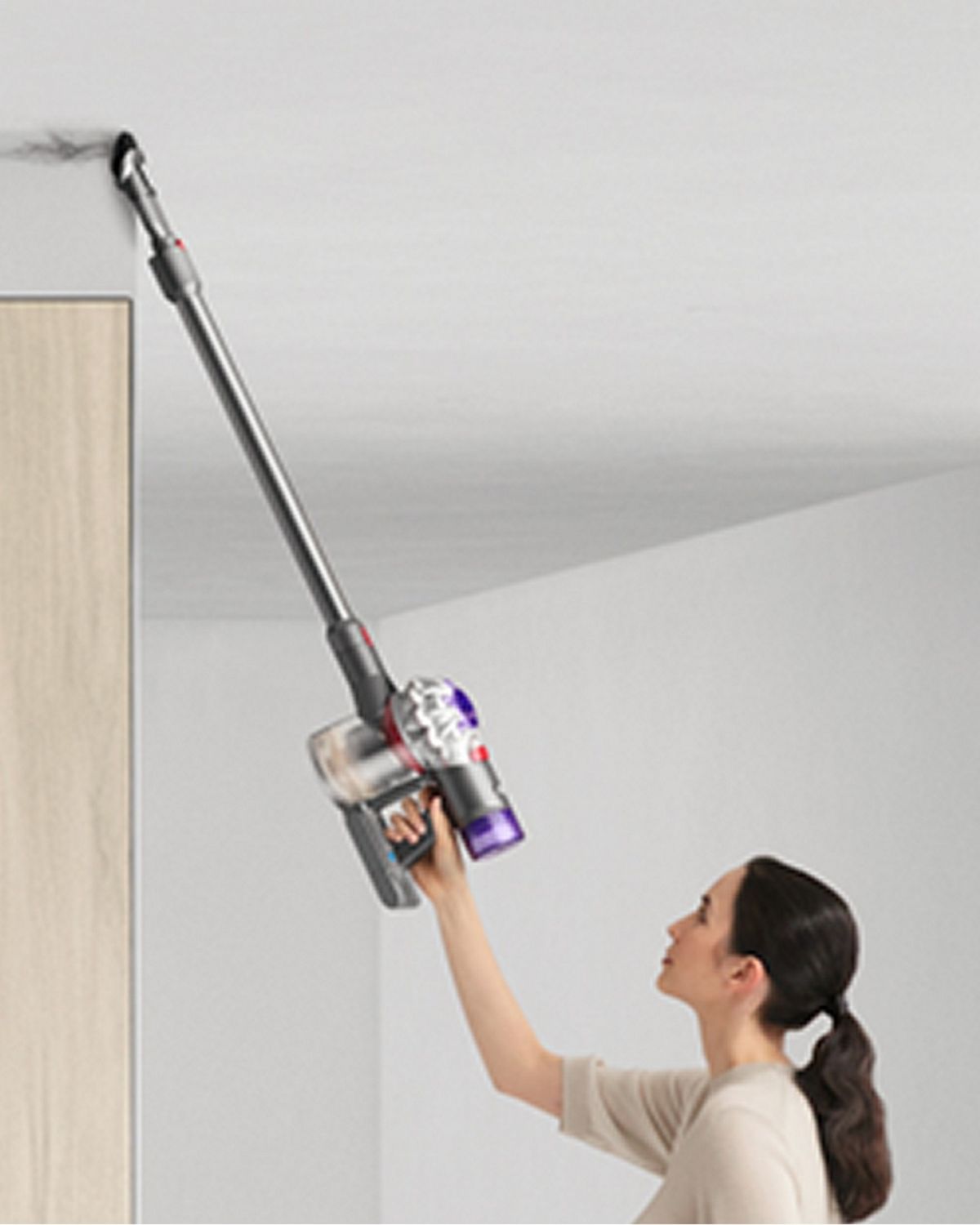 A woman using the Dyson V8 vacuum to clean a ceiling using the Combination tool.