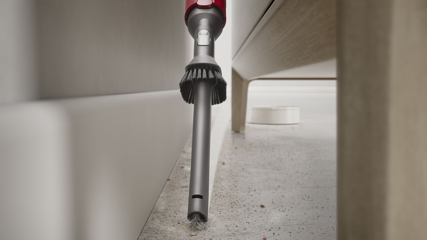 Dyson vacuum combination tool cleaning dust from a narrow gap under furniture.