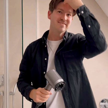 Una persona arriccia i capelli con l’asciugacapelli Dyson Supersonic, il beccuccio concentratore e la spazzola.