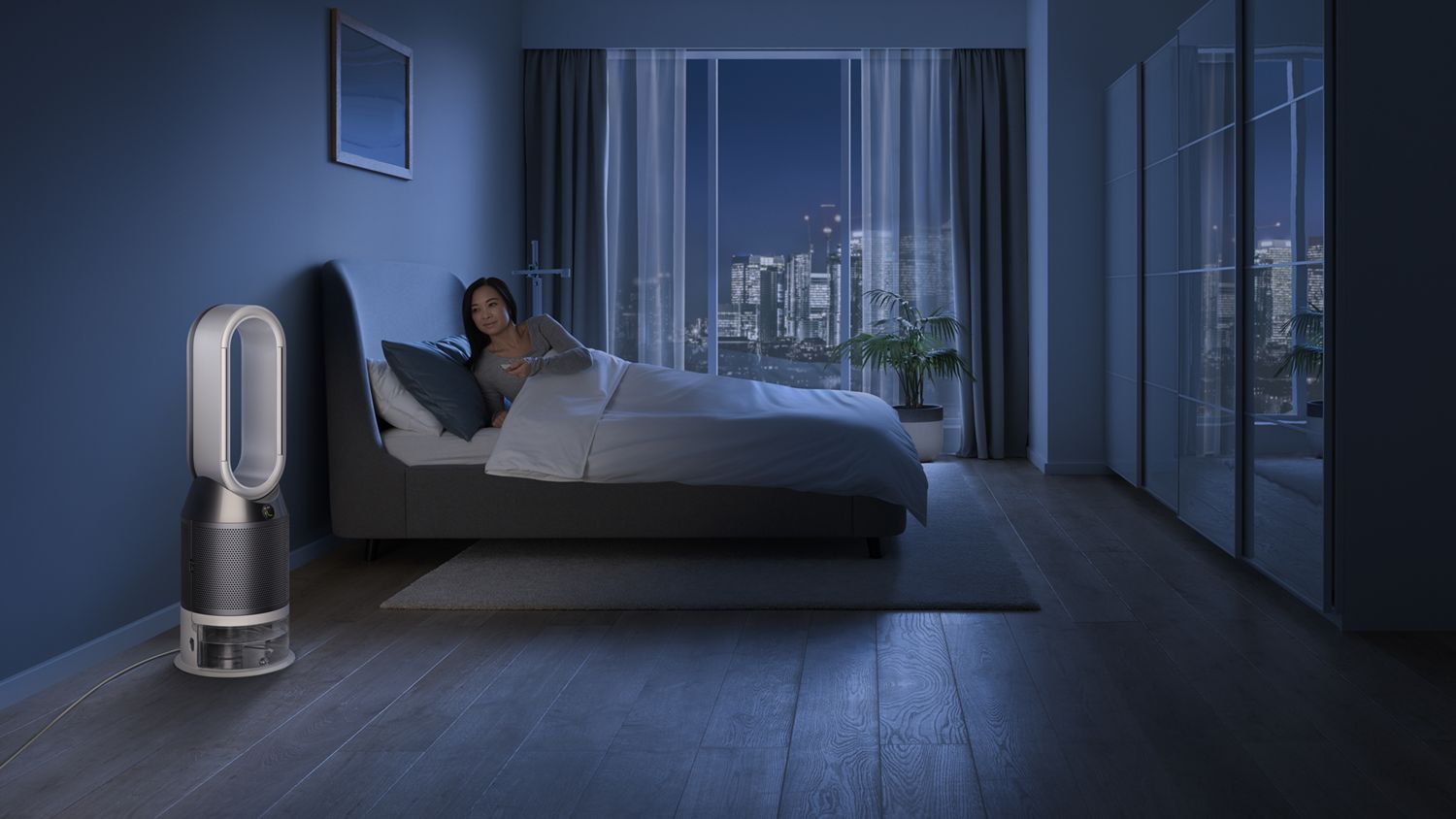 Une femme sur un lit utilise la télécommande pour éteindre le Dyson Pure Humidify+Cool. 