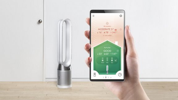 A user holding up the Dyson Link App to control their Dyson Pure Cool purifier fan in the background. 
