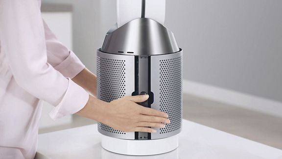 A user pressing in the sides of a Dyson Pure Cool purifier fan's filter cage, to release the filter. 