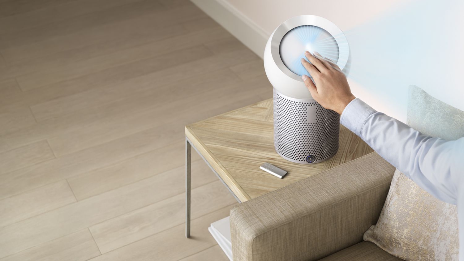 Un utilisateur ajuste la position du dôme du ventilateur purificateur personnel Dyson Pure Cool Me posé sur une table d’appui afin de réorienter le flux d’air pendant qu’il est assis sur le canapé. 