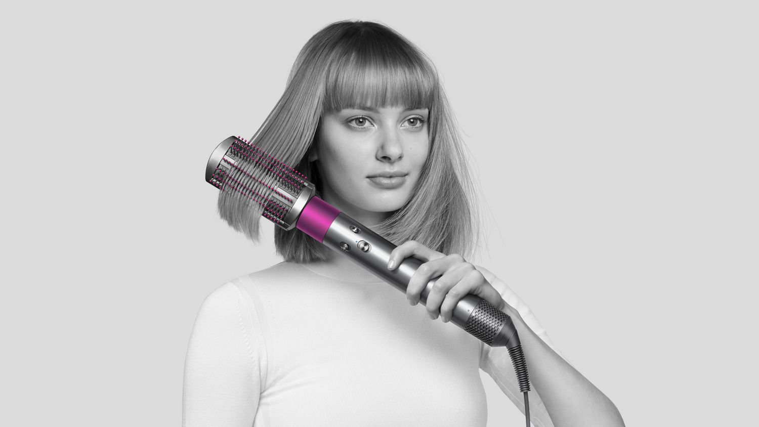 Woman using Dyson Airwrap styler with soft smoothing brush attached. 