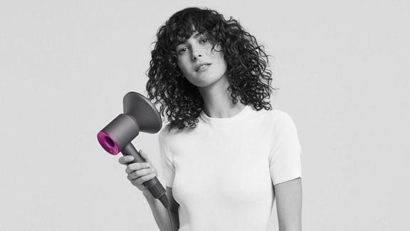 Woman holding Dyson Supersonic hair dryer with diffuser attached.