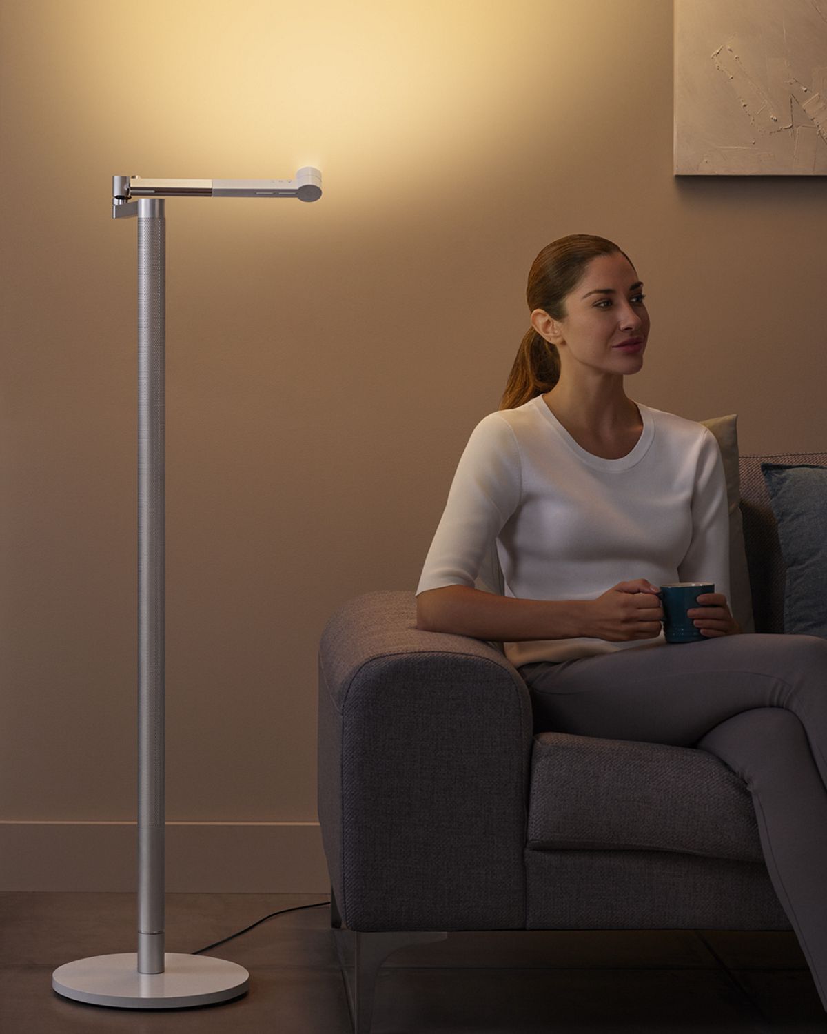 Woman sits under Dyson lightcycle morph as it lights space above her. 