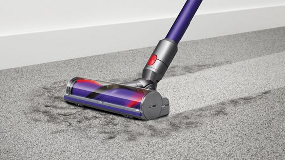 Dyson V10™ Animal kabelloser Staubsauger entfernt Schmutz von einem Teppichboden.