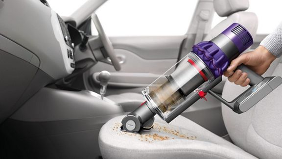Dyson V10™ Animal kabelloser Staubsauger im Handheld-Modus entfernt Schmutz von einem Autositz.
