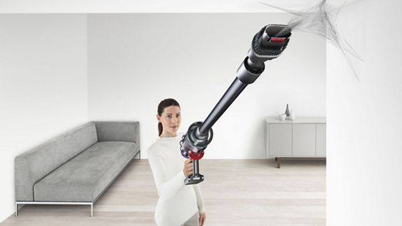 Ein Dyson V10 Total Clean kabelloser Staubsauger entfernt Spinngewebe von einer schwierig zu erreichenden Stelle an der Decke