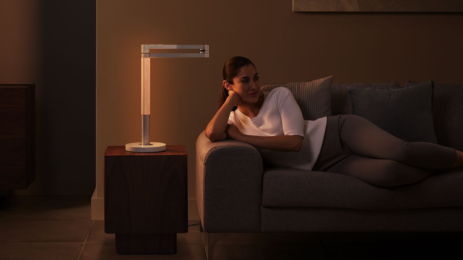 Una donna che si rilassa sul divano con la luce Dyson Morph rivolta verso il suo stelo traforato, creando un ambiente e un bagliore caldo.