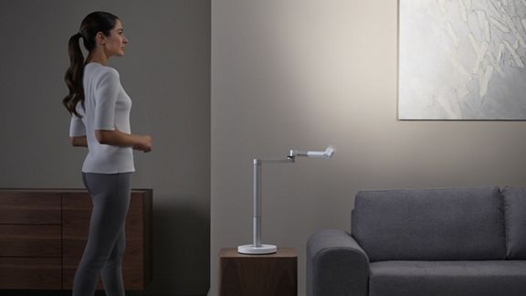 Die Dyson Solarcycle Morph™ Tischleuchte ist auf die Wand gerichtet, beleuchtet ein Gemälde und kreiert indirektes Licht im Raum. 