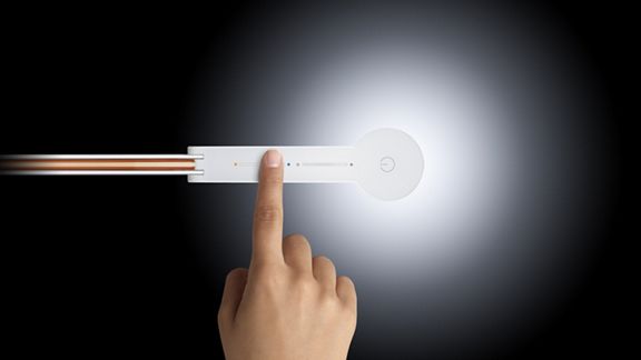 Ein Benutzer hält die Dyson Link App hoch, um die Dyson Solarcycle™ Leuchte im Hintergrund zu steuern. 