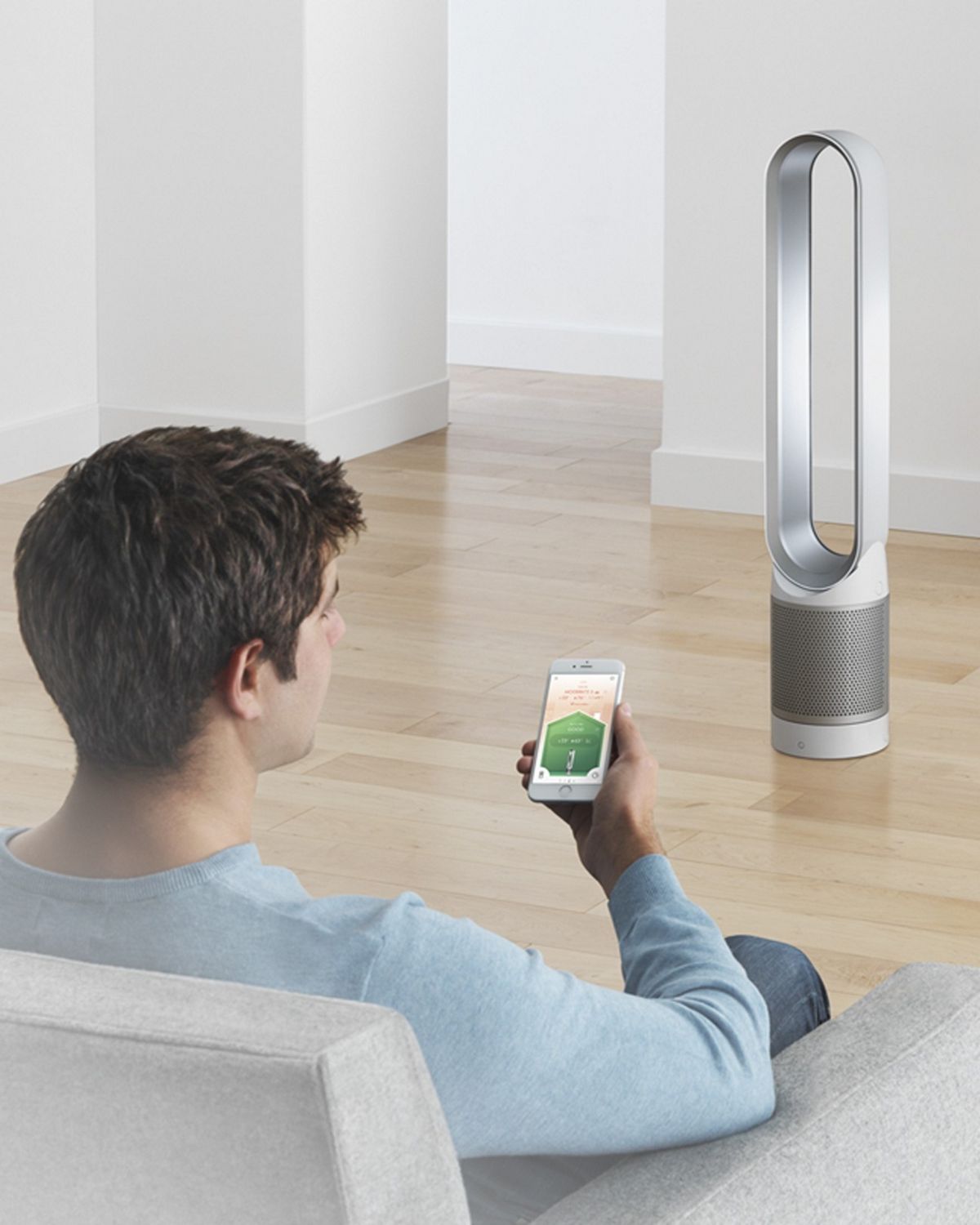 A person looking at their Dyson Link app to control their Dyson Pure Cool purifier fan in the background. 