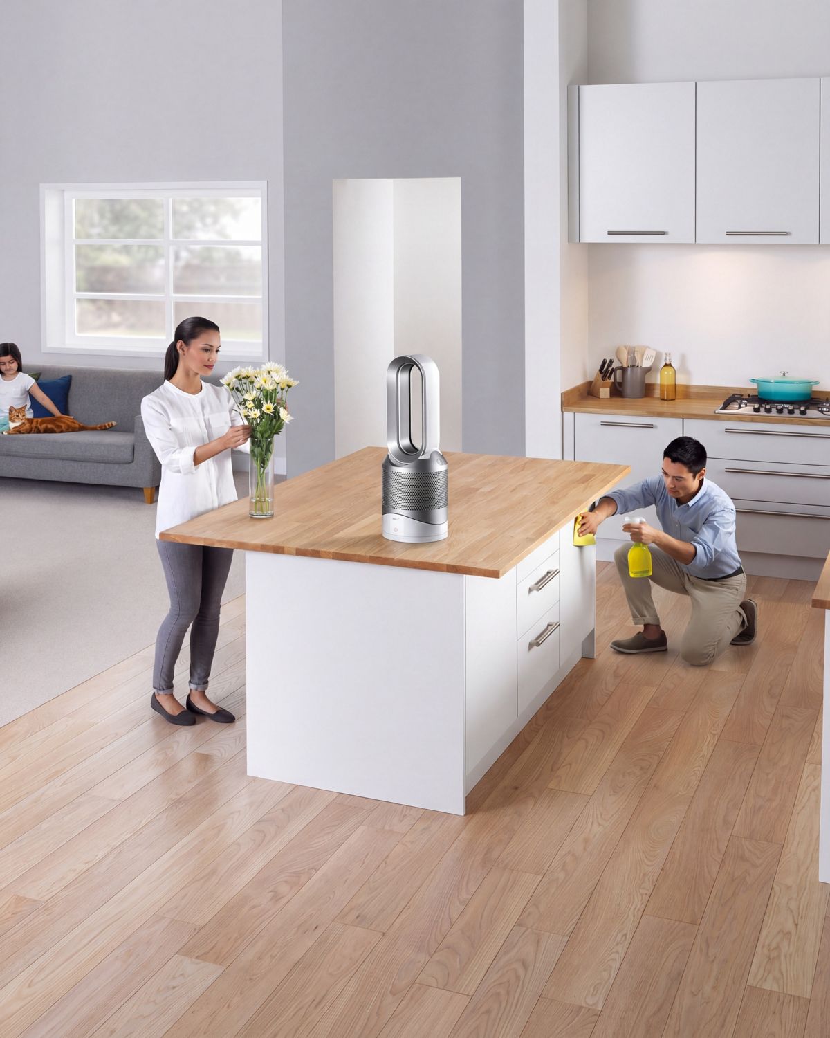 A Dyson Pure Hot+Cool purifier fan heater in the middle of a kitchen as someone arranges flowers and cleans the worksurfaces. 