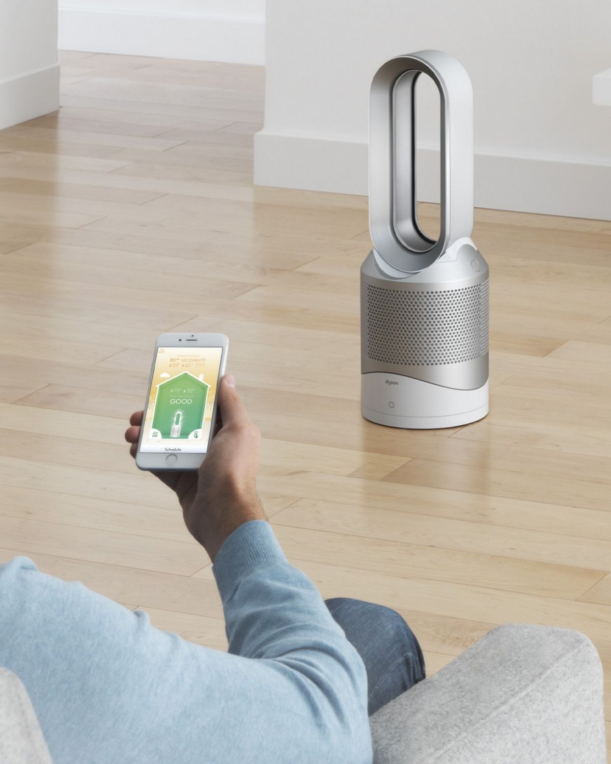 A man looks at his Dyson Link App to control his Dyson Pure Hot+Cool purifier fan in the background. 