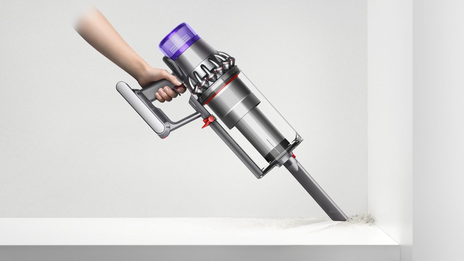 A Dyson V11 Outsize cordless vacuum cleaner with attachment cleaning debris from a shelf corner