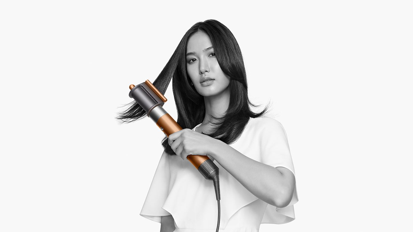 Woman smoothing flyaways with the Dyson Airwrap Complete pre-styling dryer
