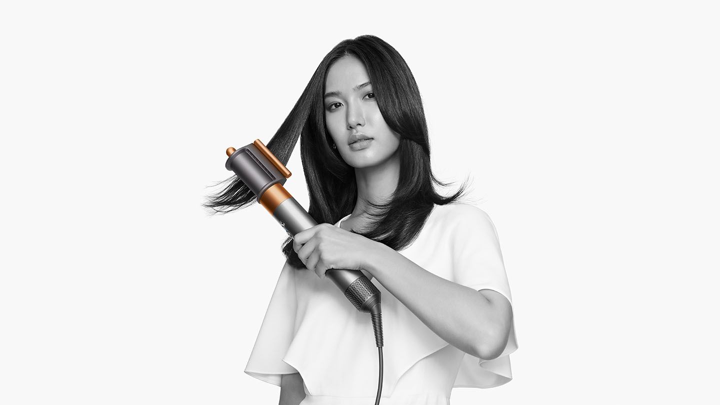 Woman smoothing flyaways with the Dyson Airwrap Complete pre-styling dryer