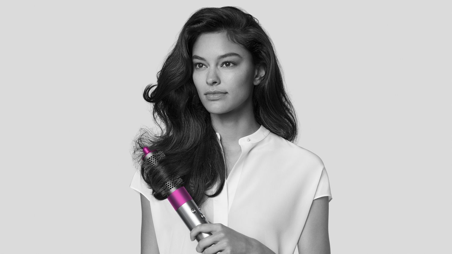 Woman using Dyson Airwrap styler with round volumizing brush attached. 
