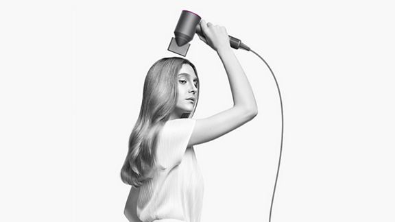 Woman holding Dyson Supersonic hair dryer with styling concentrator attachmentt