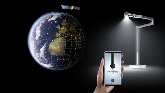 The Dyson Link app, with the Dyson Lightcycle Morph light in the background, next to a picture of the globe showing the time and date lines. 