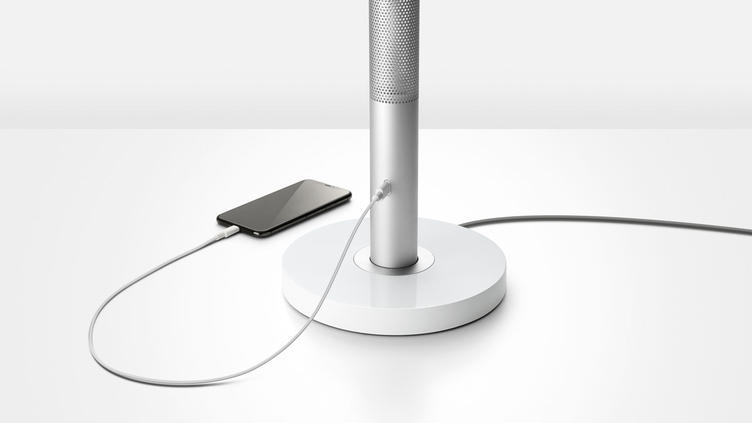 A mobile phone plugged into the charging point on the base of the Dyson Lightcycle Morph light. 