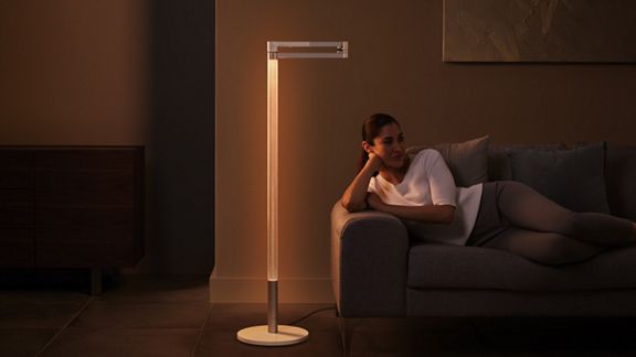 A woman relaxing on the sofa with the Dyson Morph light set with its light facing into its perforated stem, creating an ambient and warm glow. 