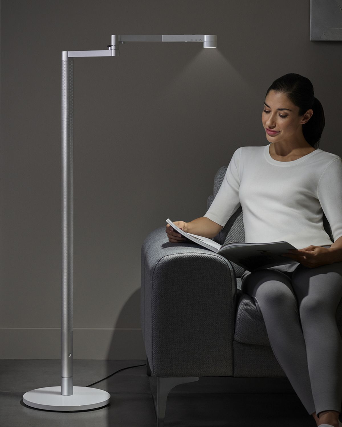 A woman reading her book, with the Dyson Lightcycle Morph light positioned over her page. 