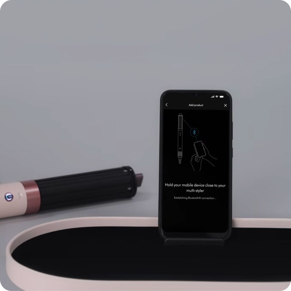 Dyson Airwrap multi-styler with a phone showing the MyDyson app.