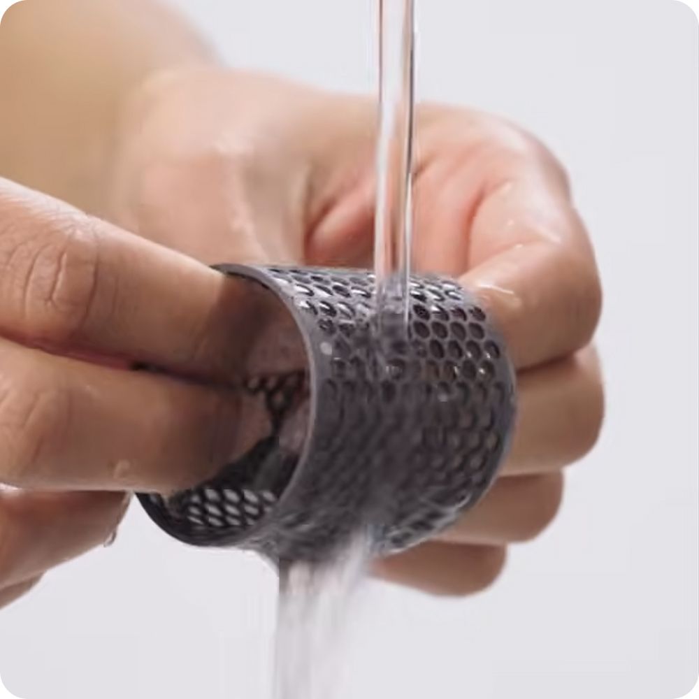 A Dyson Airwrap filter is rinsed under running water.