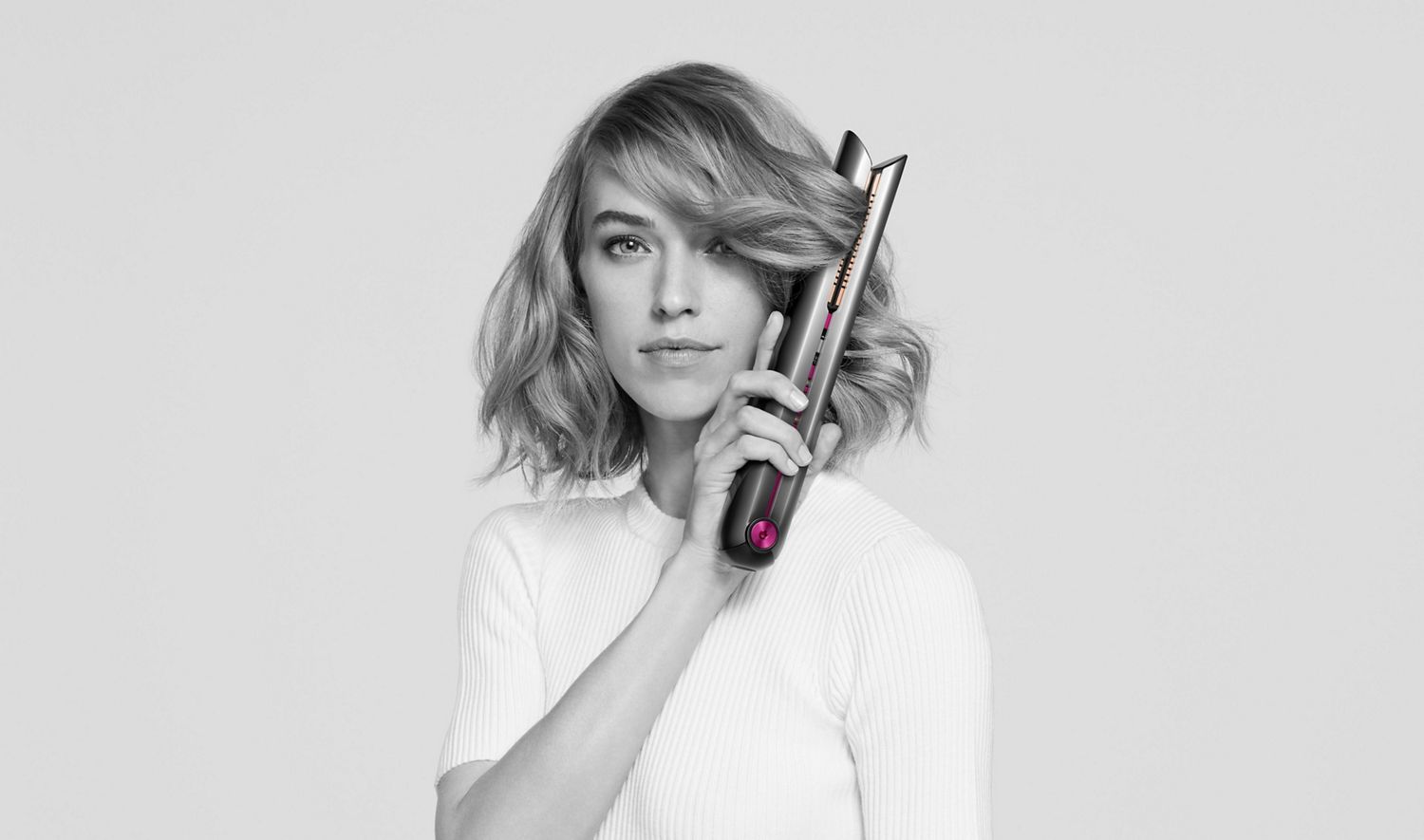 A model looking at camera while using the Dyson Corrale hair straightener on her short hair.