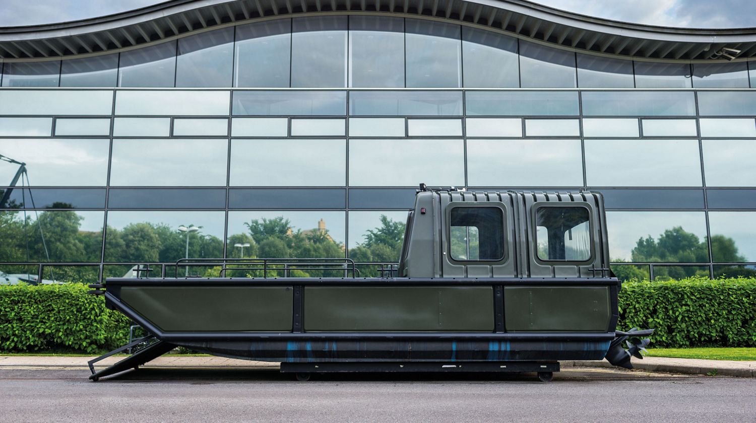 Side view of the Sea Truck in front of the wavy-roofed main building on the Dyson campus in Malmesbury.