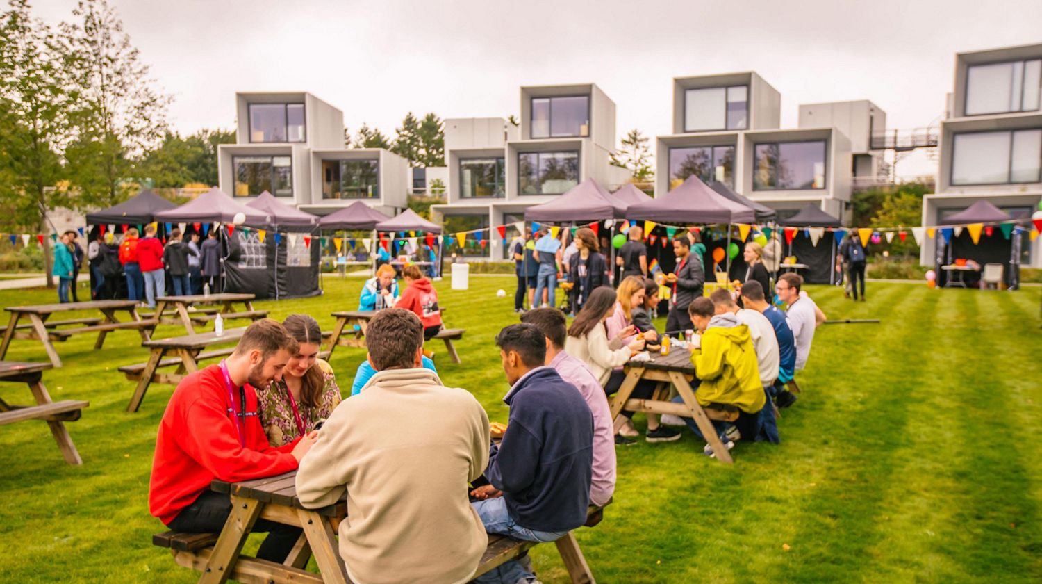 Wide view of students at picnic tables in front of the Undergraduate Village. 