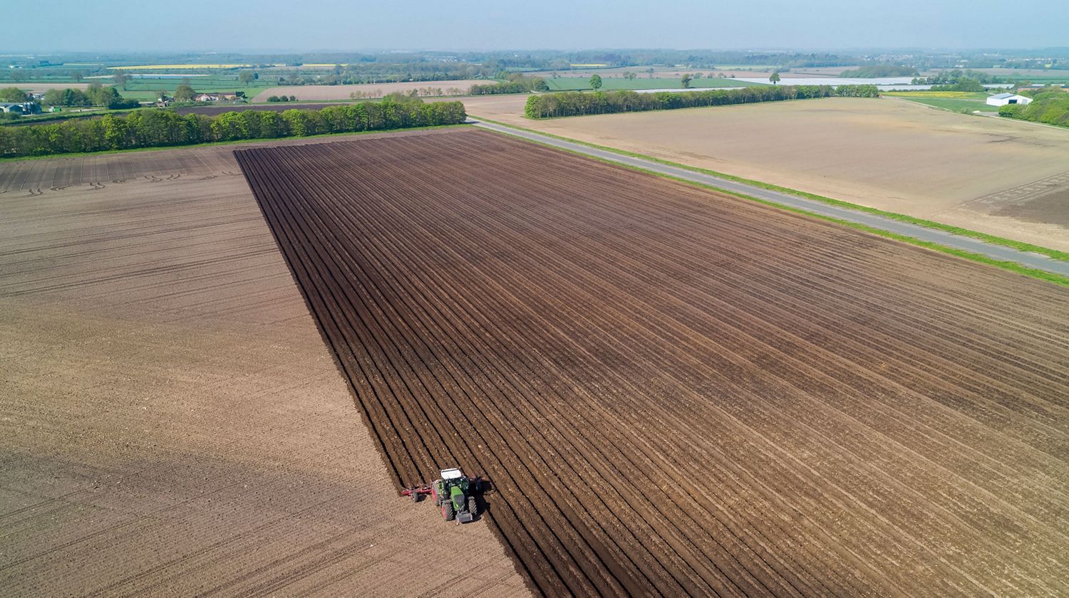 A long shot of a perfectly-ploughed field and tractor.